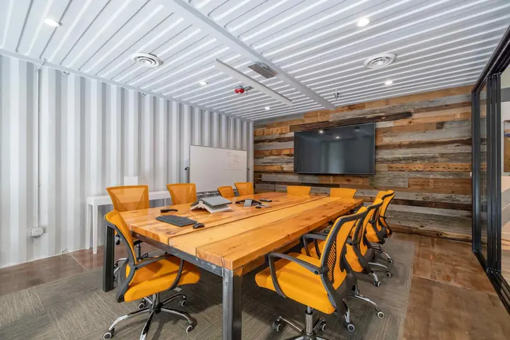 Container conference room with white corrugated walls, reclaimed wood accent wall, wall-mounted TV and wood table