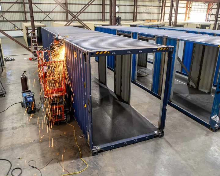 Welder on a scissor lift cutting a shipping container sidewall with sparks flying
