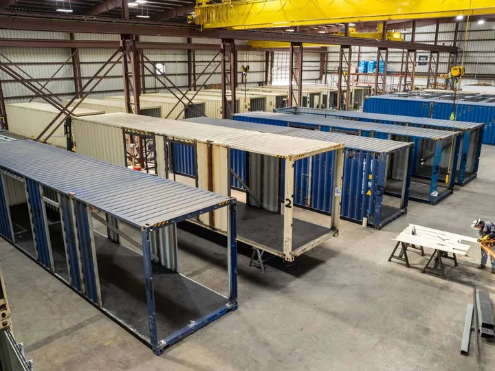 Shipping containers in a fabrication shop with sidewalls cut out and steel framing added