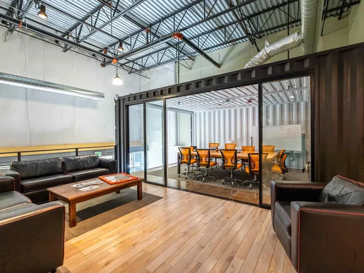 Glass-front container conference room on a mezzanine next to a lounge area