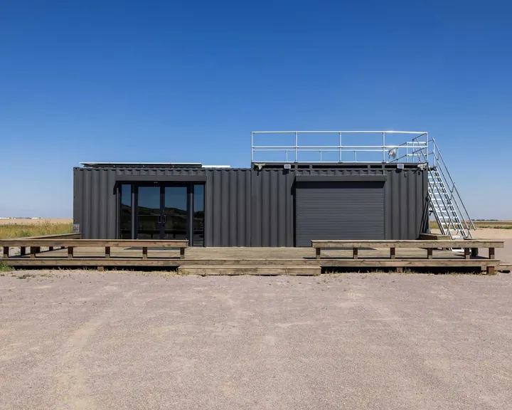Finished container site office with glass double doors, roll-up door, wraparound wood deck and rooftop deck with railing