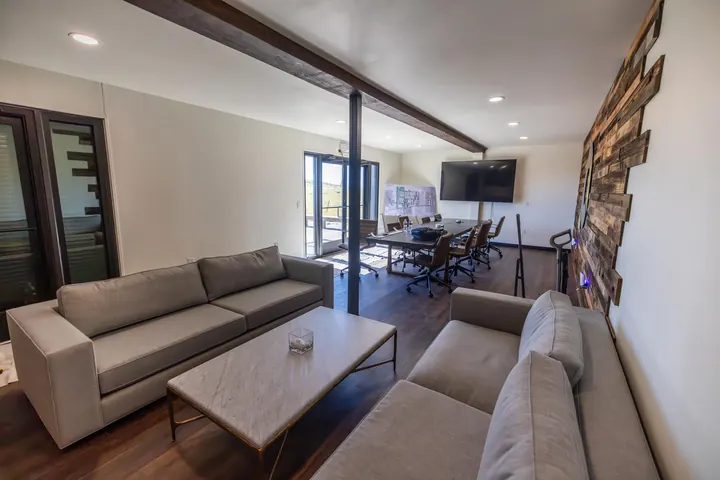 Open container office with lounge seating, exposed wood beam, conference table and wall-mounted TV