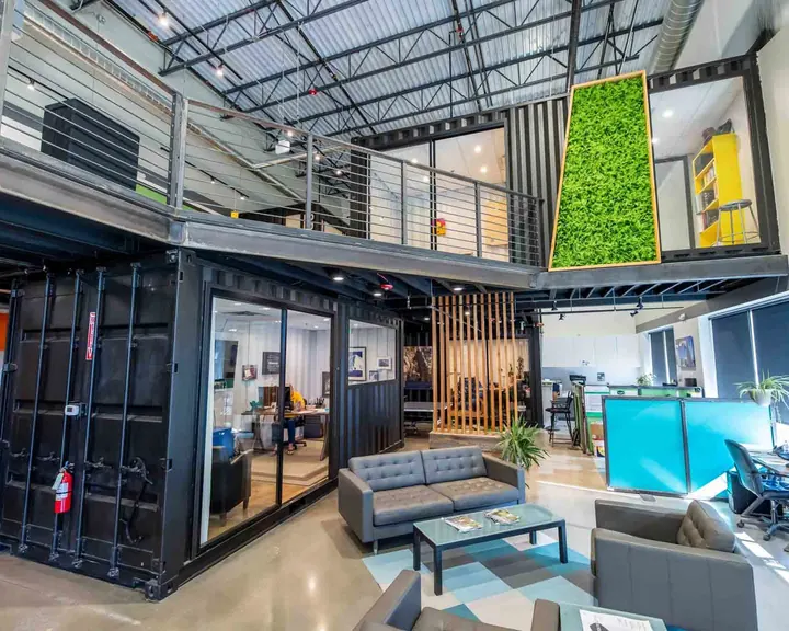 Two-story container office build inside a warehouse with mezzanine walkway, moss wall and glass-front offices