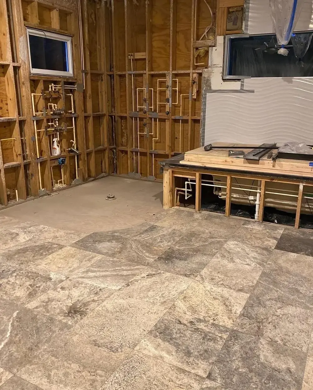Bathroom stripped to studs with rough plumbing set and subfloor tile started, before remodel