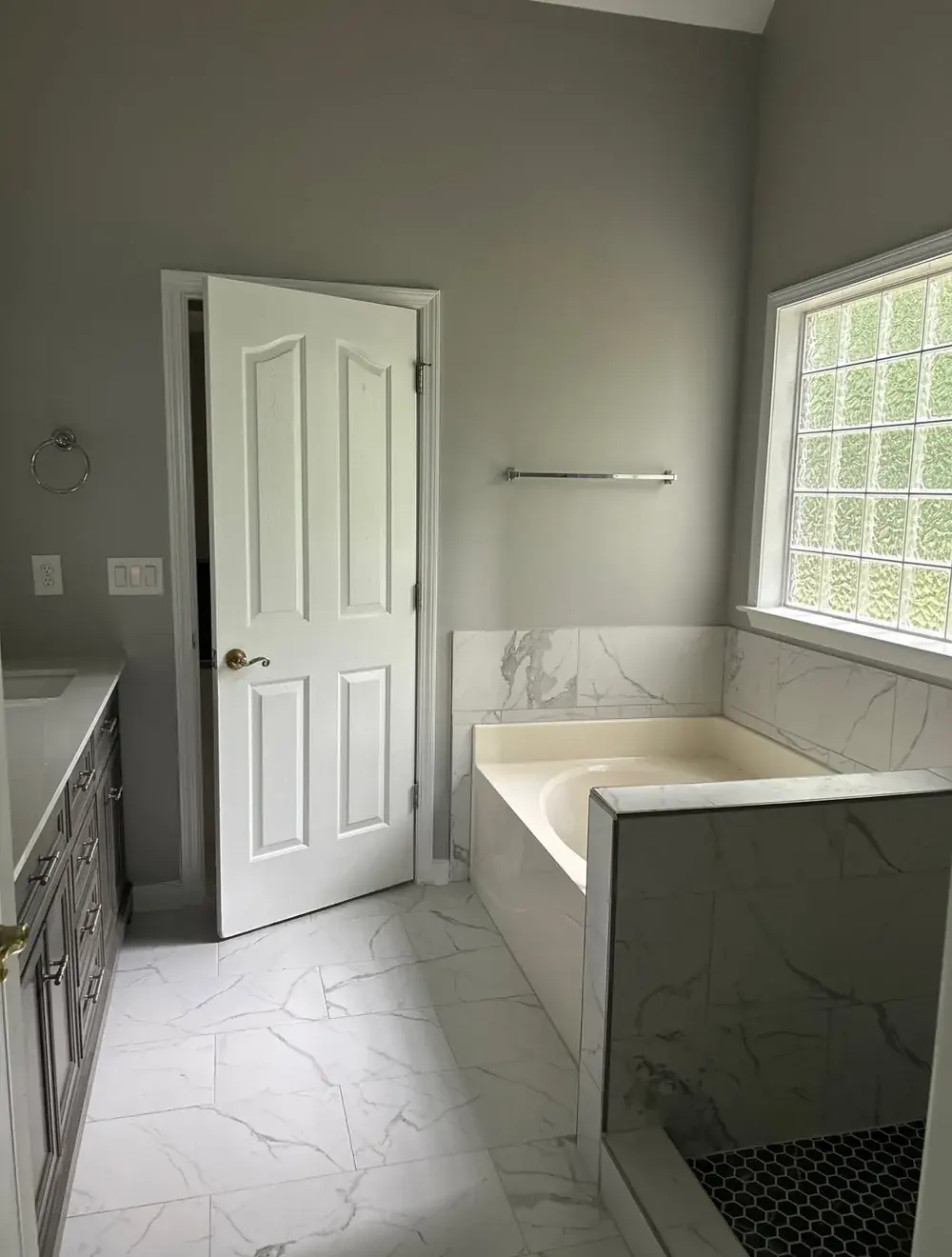 Finished bathroom with gray paint, marble-look tile flooring, marble-tiled tub deck, and glass-enclosed hex-tile shower