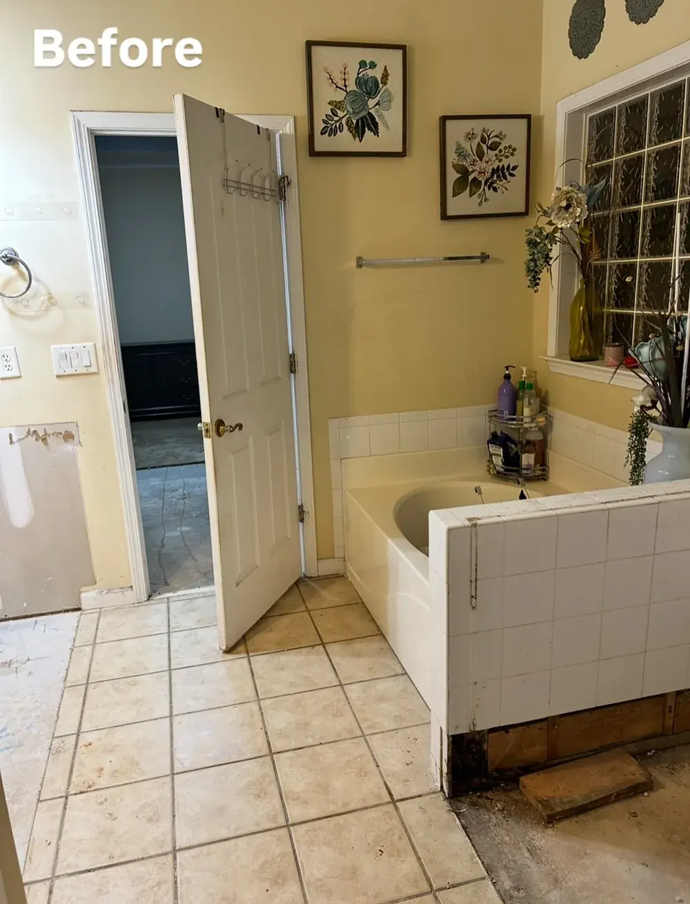 Primary bathroom mid-demolition with yellow walls, old tile flooring, exposed subfloor, and damaged tub surround