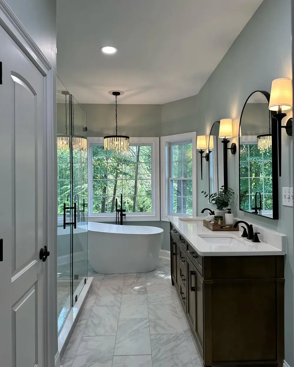 Finished spa-style primary bathroom with freestanding soaking tub, dark wood double vanity, quartz counters, matte black fixtures, and chandelier lighting