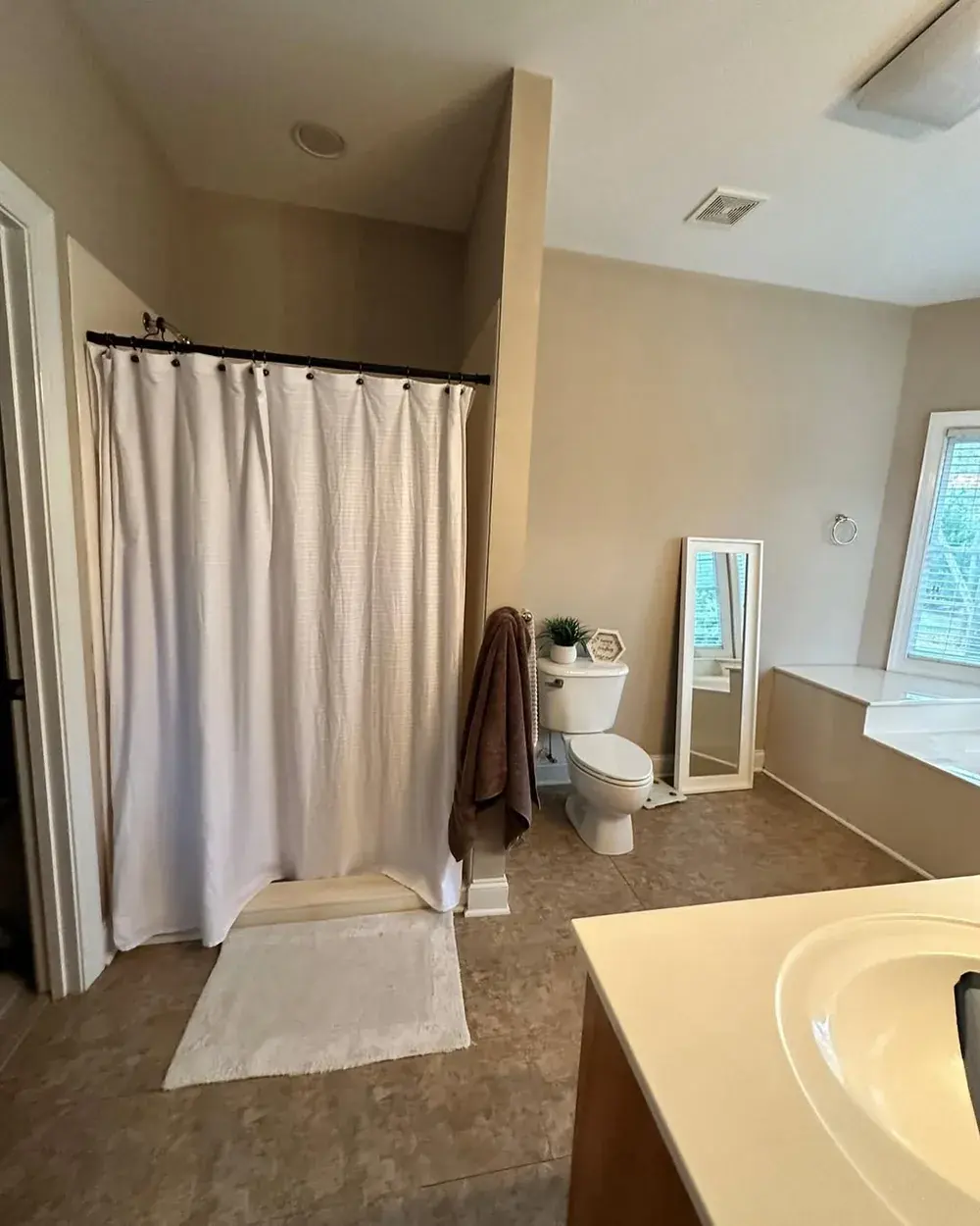 Original shower with cream shower curtain and dated tile floor before remodel