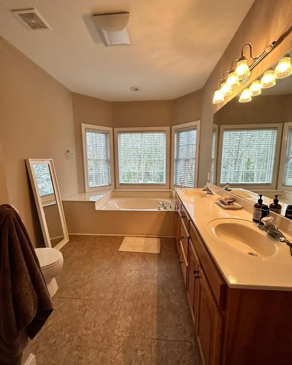 Dated primary bathroom with garden tub, oak vanity, cultured marble counters, and worn tile floor before remodel