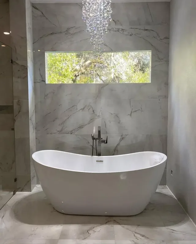 Freestanding soaking tub set against a marble accent wall