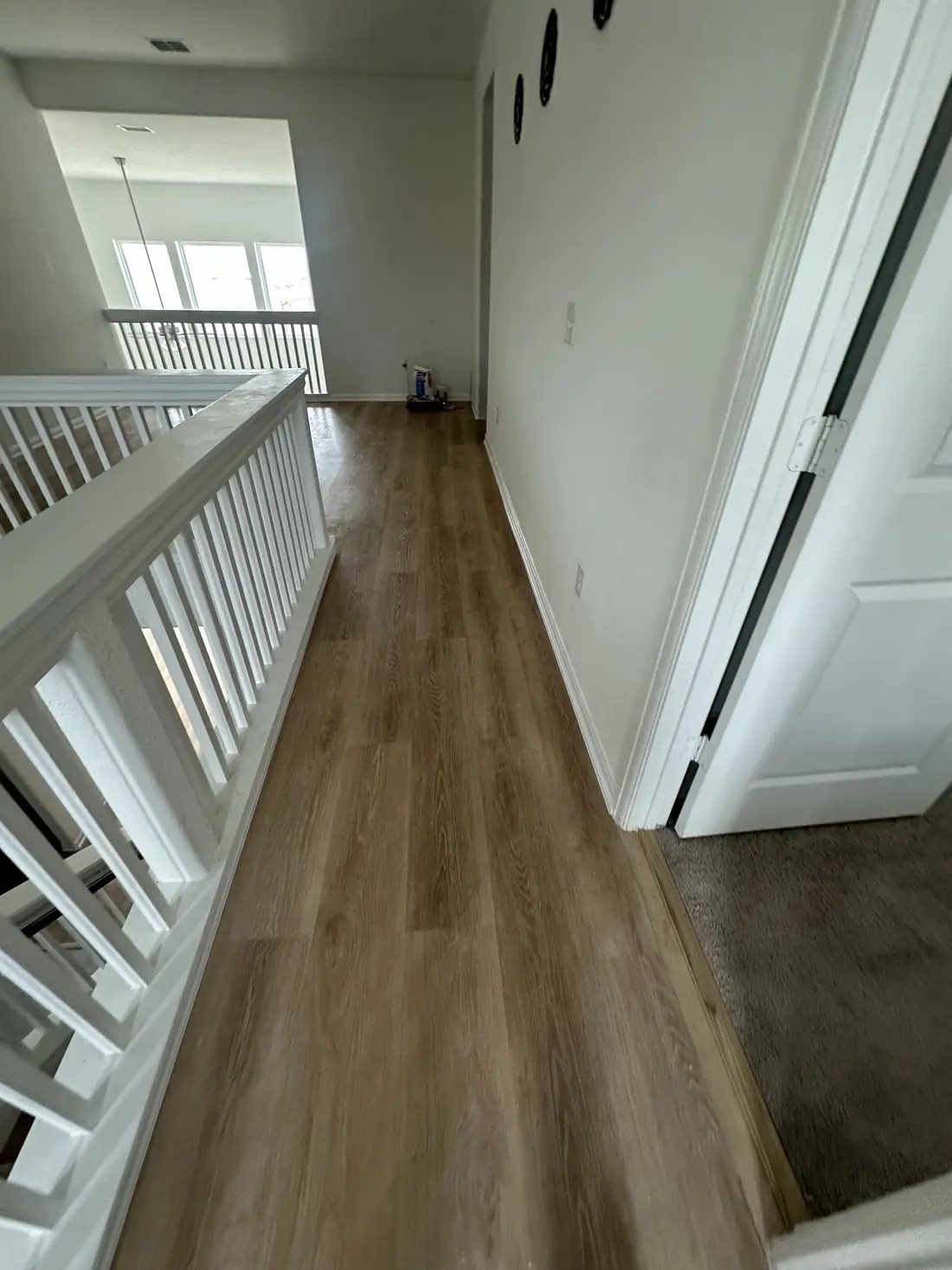 Upstairs hallway view down the staircase landing showing new wood-look flooring next to the stairwell railing