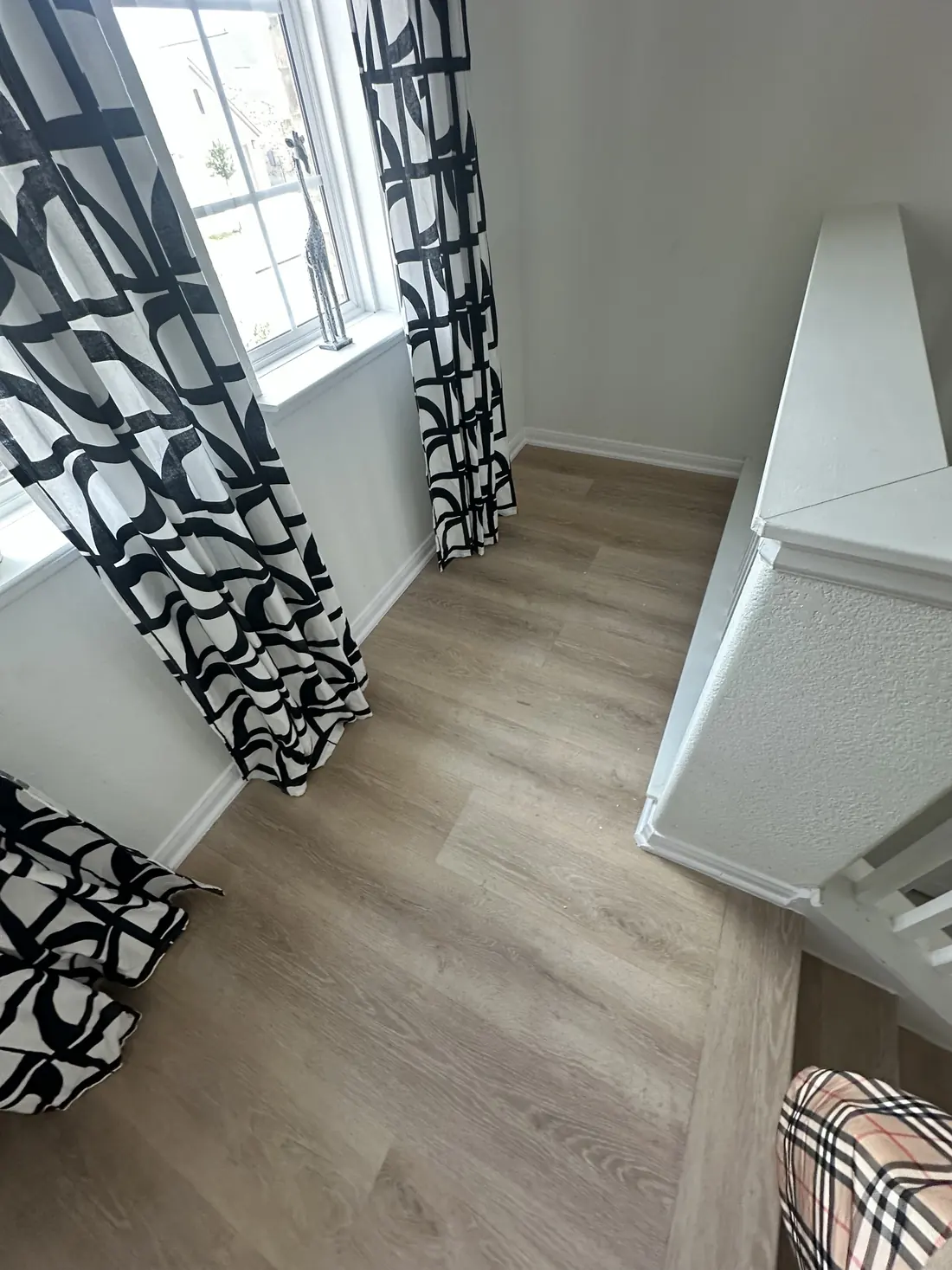 Upstairs hallway with new wood-look flooring leading past a window and dresser
