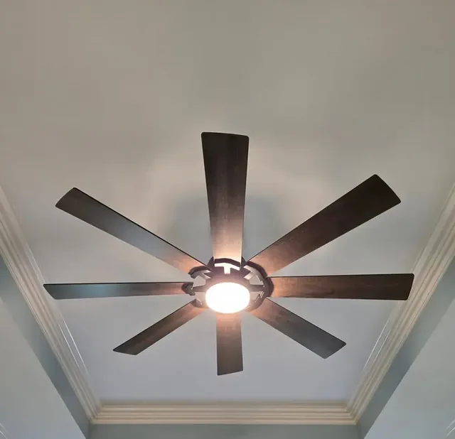 Large 8-blade wood-look ceiling fan with light installed on a vaulted, crown-molded ceiling