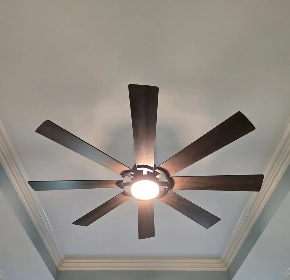 Large 8-blade wood-look ceiling fan with light installed on a vaulted, crown-molded ceiling
