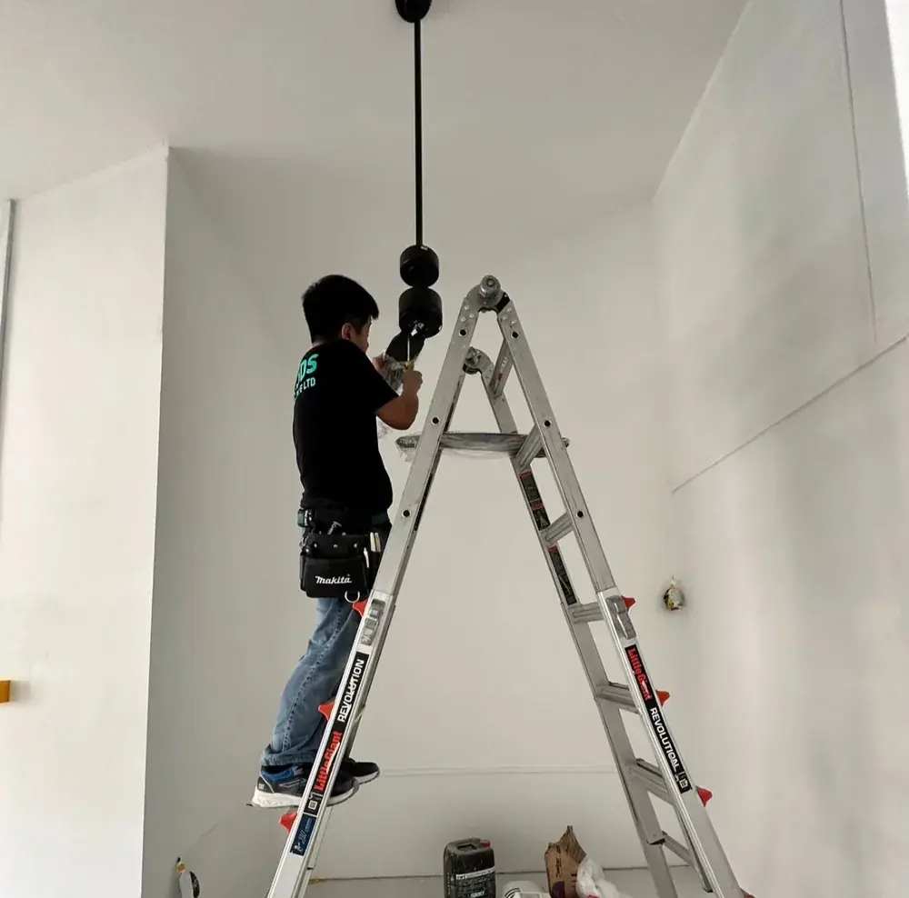 Installer on a ladder wiring a black downrod ceiling fan mount