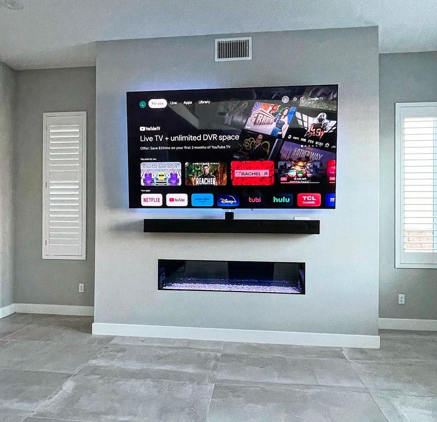 Wide view of a mounted TV, soundbar, and fireplace niche on the same media wall