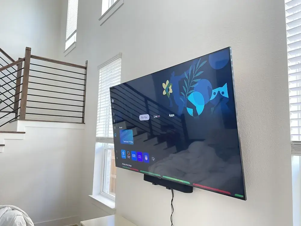 TV on a full-motion mount below a vaulted ceiling and staircase, soundbar mounted underneath