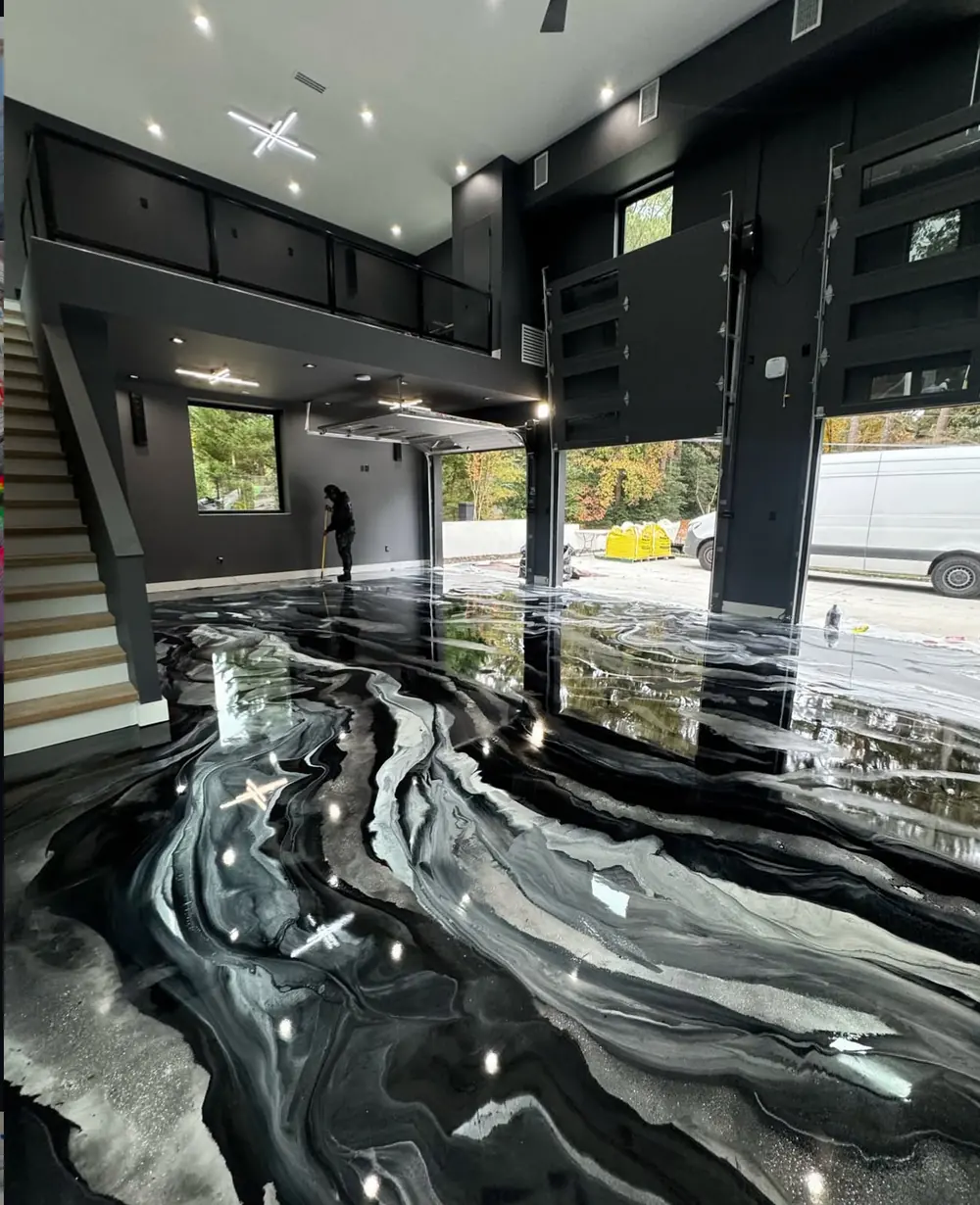 Black, gray, and white marbled metallic epoxy floor coating in a two-story modern garage with a loft above