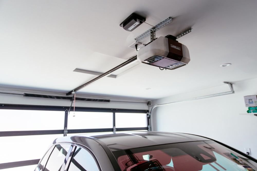 Garage door opener mounted to the ceiling with the drive rail set and a car parked below