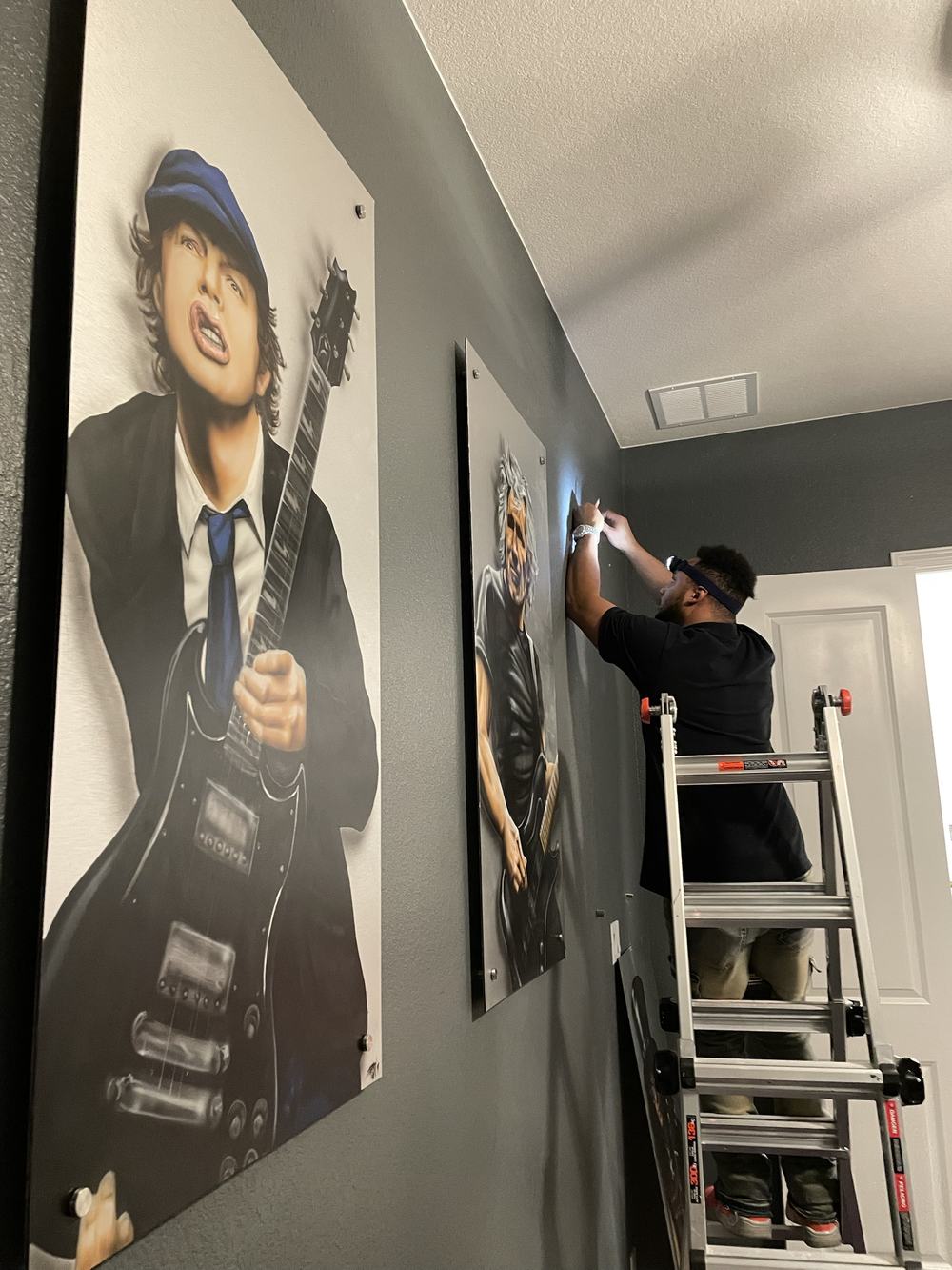 Installer on a ladder hanging matching guitarist art panels along a hallway wall