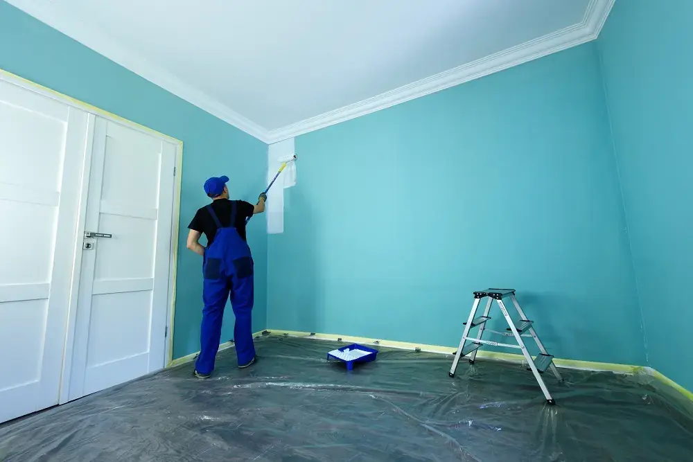 Painter rolling teal paint onto bedroom walls with crown molding taped off
