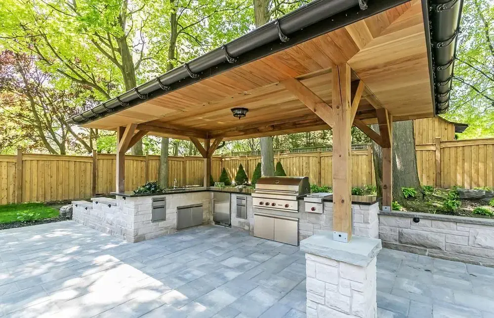 Covered timber-frame pavilion with a stone outdoor kitchen underneath