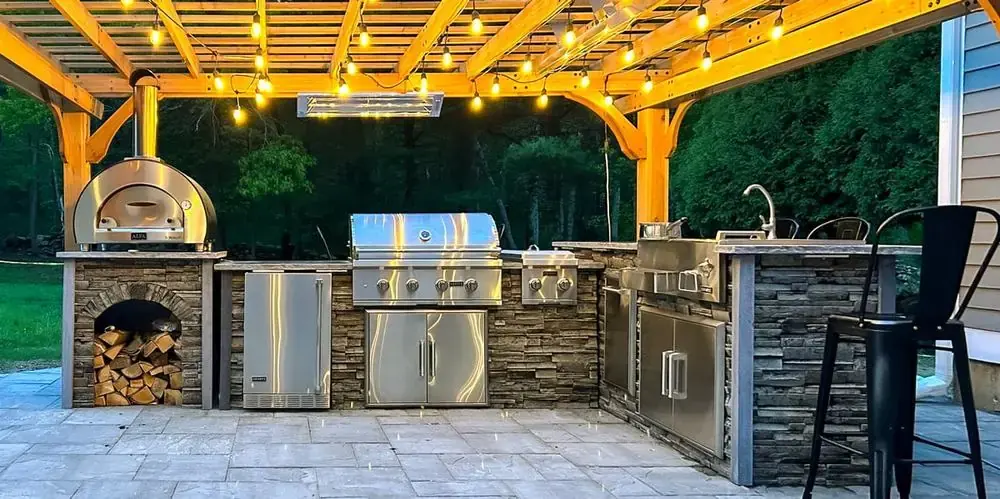 Stone outdoor kitchen with a built-in pizza oven under a string-lit pergola